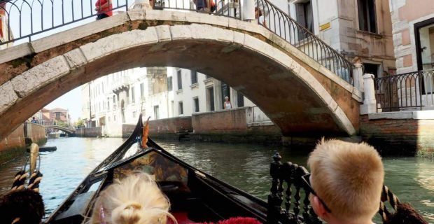 Happy kids on a gondola tour under a bridge in Venice, Italy